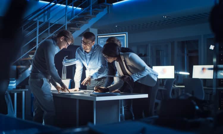 Diverse Team of Electronics Development Engineers Standing at the Desk Working with Documents, Solving Project Problems Late at Night. Specialists Working on Ultra Modern Industrial Design.